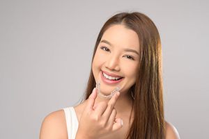 Happy young woman holding Invisalign aligner close to her mouth