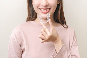 Young Invisalign patient holding aligner closer to her mouth