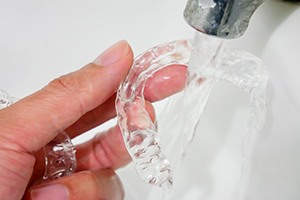 Hand holding Invisalign aligner under sink faucet